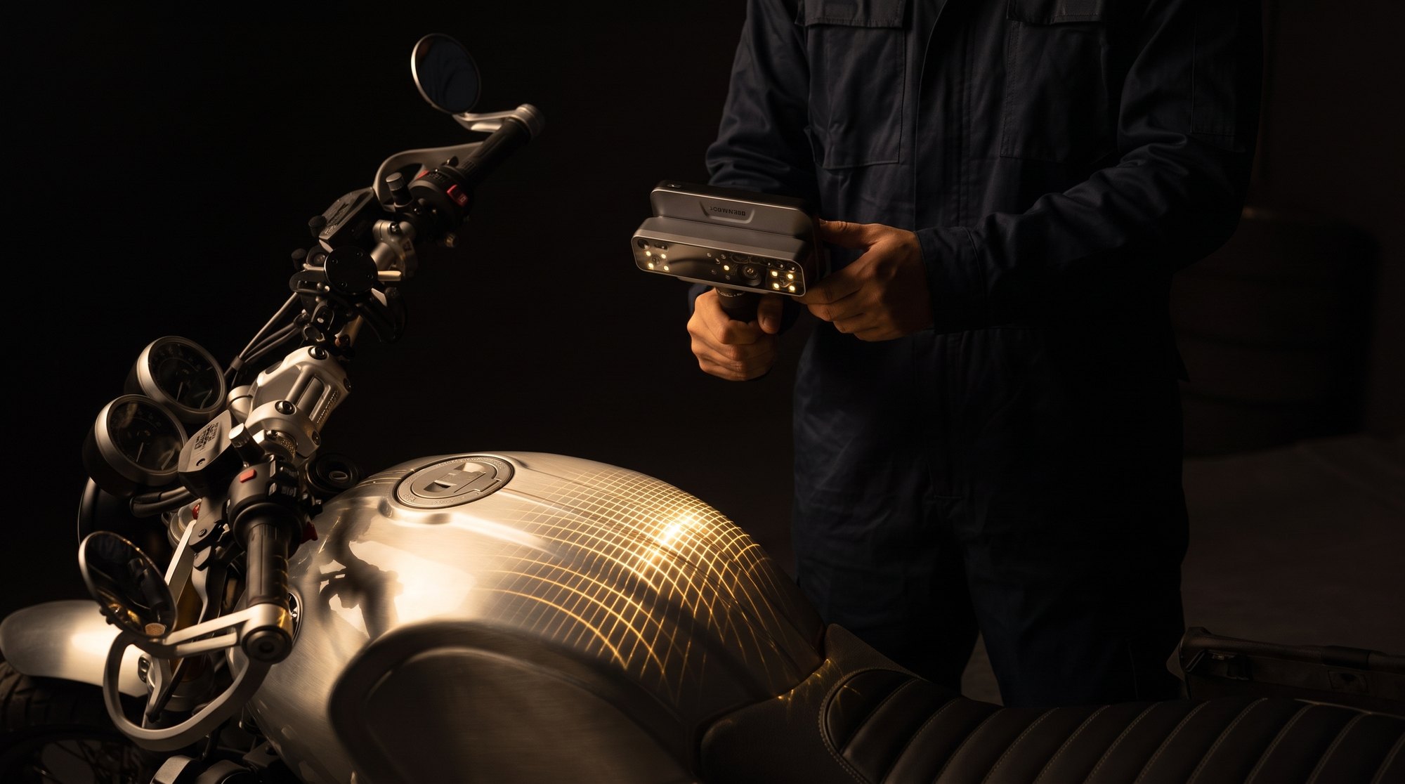 A technician scanning a motorcycle fuel tank with a handheld 3D scanner projecting a gold laser grid.